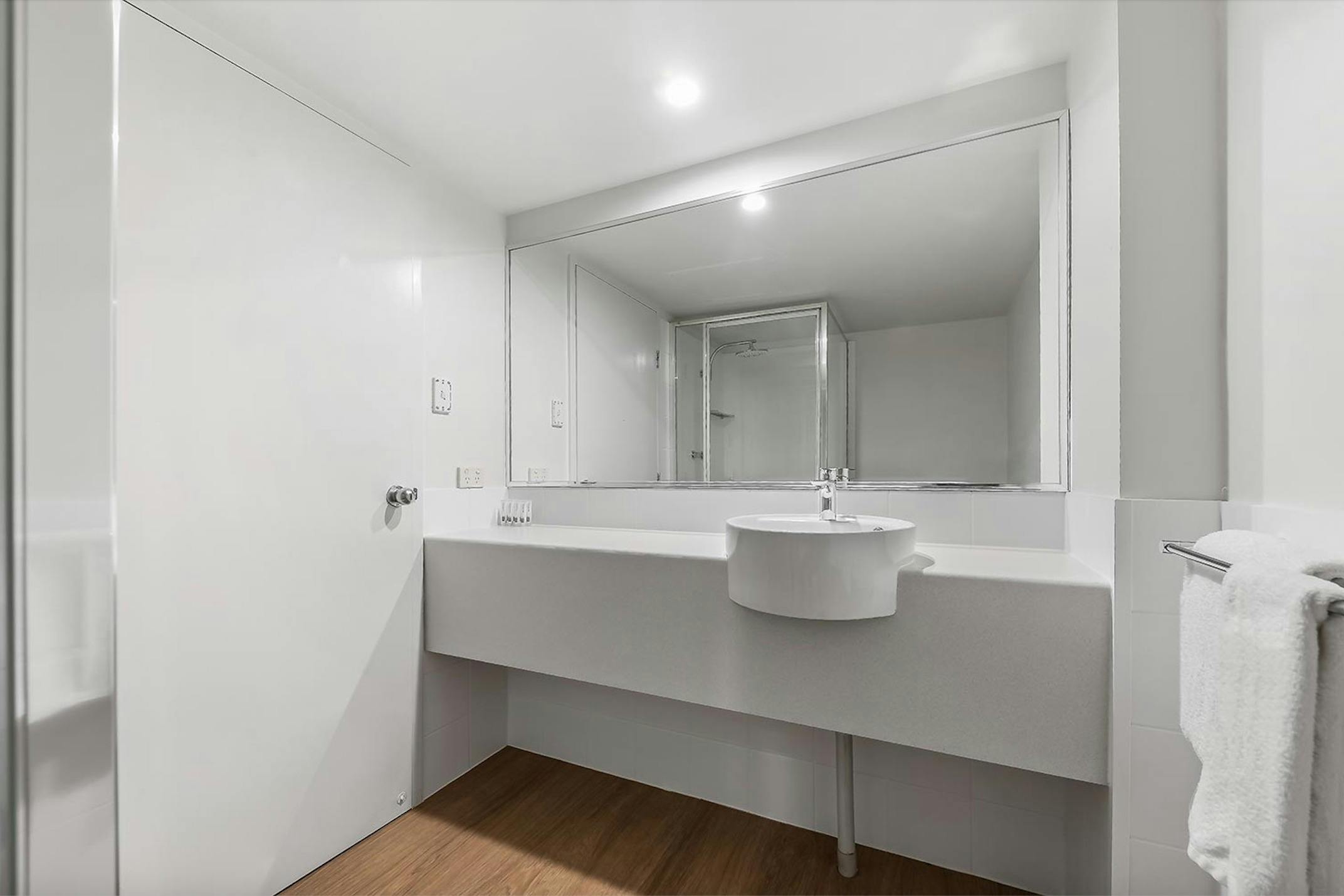 White bathroom with vanity, mirror, and shower area.