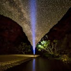 A traveller shines a torch towards the starry night sky with Simpsons Gap in the background