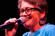 Woman smiling wearing glasses and blue tee-shirt speaking into microphone