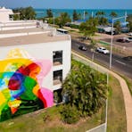 A mural with a sea view. The mural is of a woman wearing a hat, painted in primary colors.