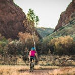A woman riding a mountain bike on the path towards Simpsons Gap