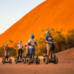 A group segways towards the camera with an amazing view of Uluru behind them