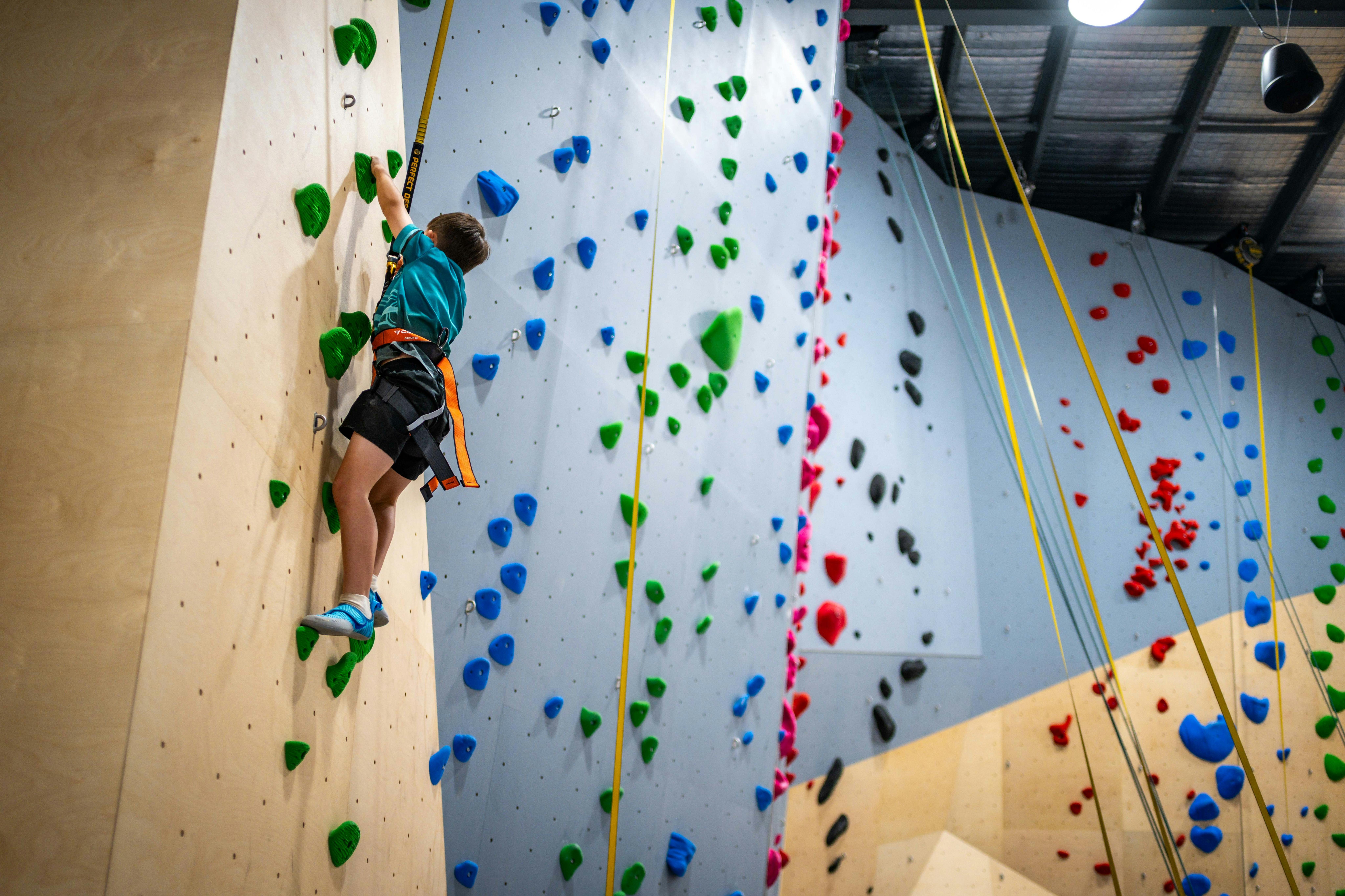 boy climbing up rock climbing wall with harness and rope