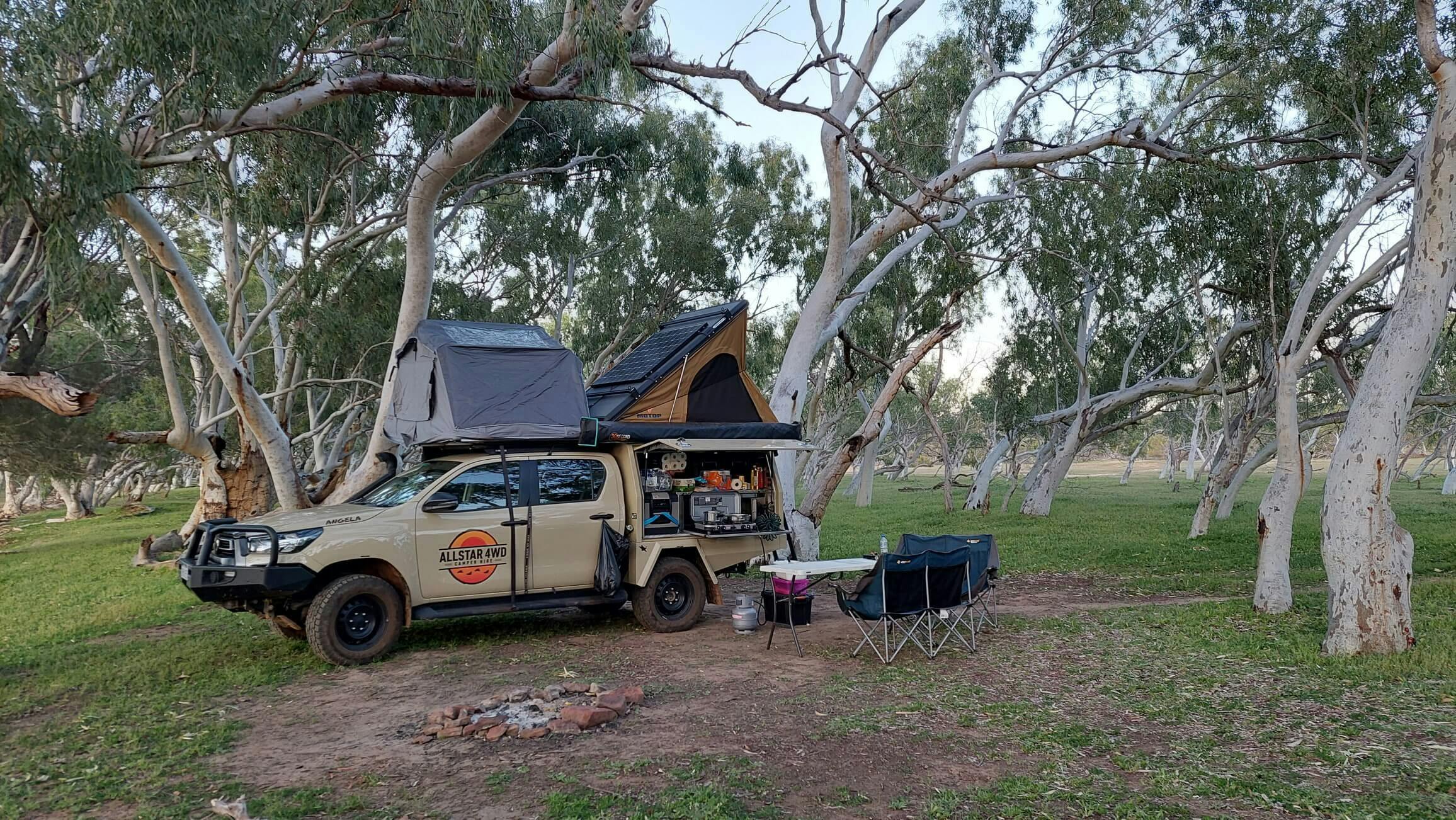 4WD camper parked in the bush with rooftop tents and chair setup.
