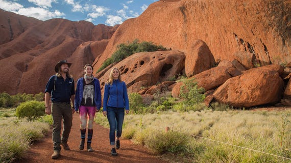 A group of people walking around the base of Uluru