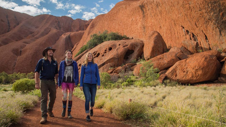 A group of people walking around the base of Uluru