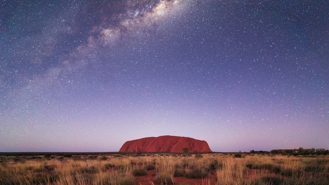 long distance shot of uluru on the horizon under the stars at night
