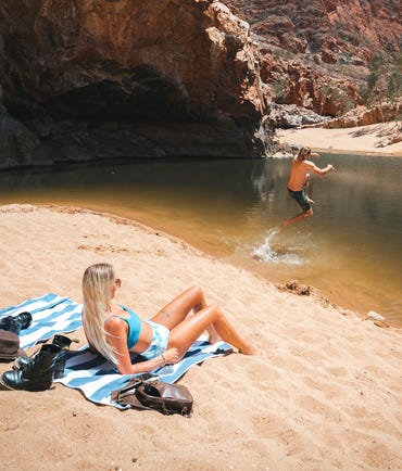 guyjumpingintothewaterholeatormistongorgewhilehisgirlfriendissunbathingonthesandyshorejpg