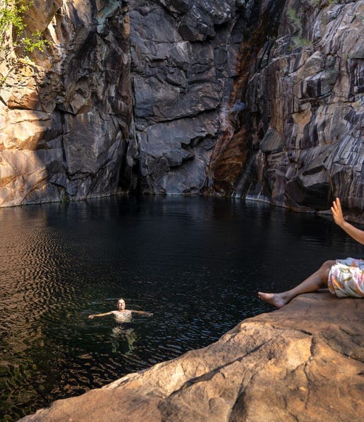 Woman taking pictures of man swimming in remote water hole