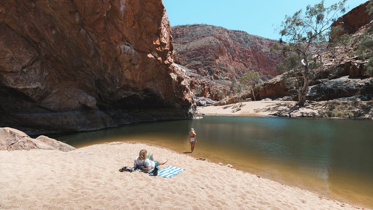 A couple relaxing on the sand by the waters edge at Ormiston Gorge