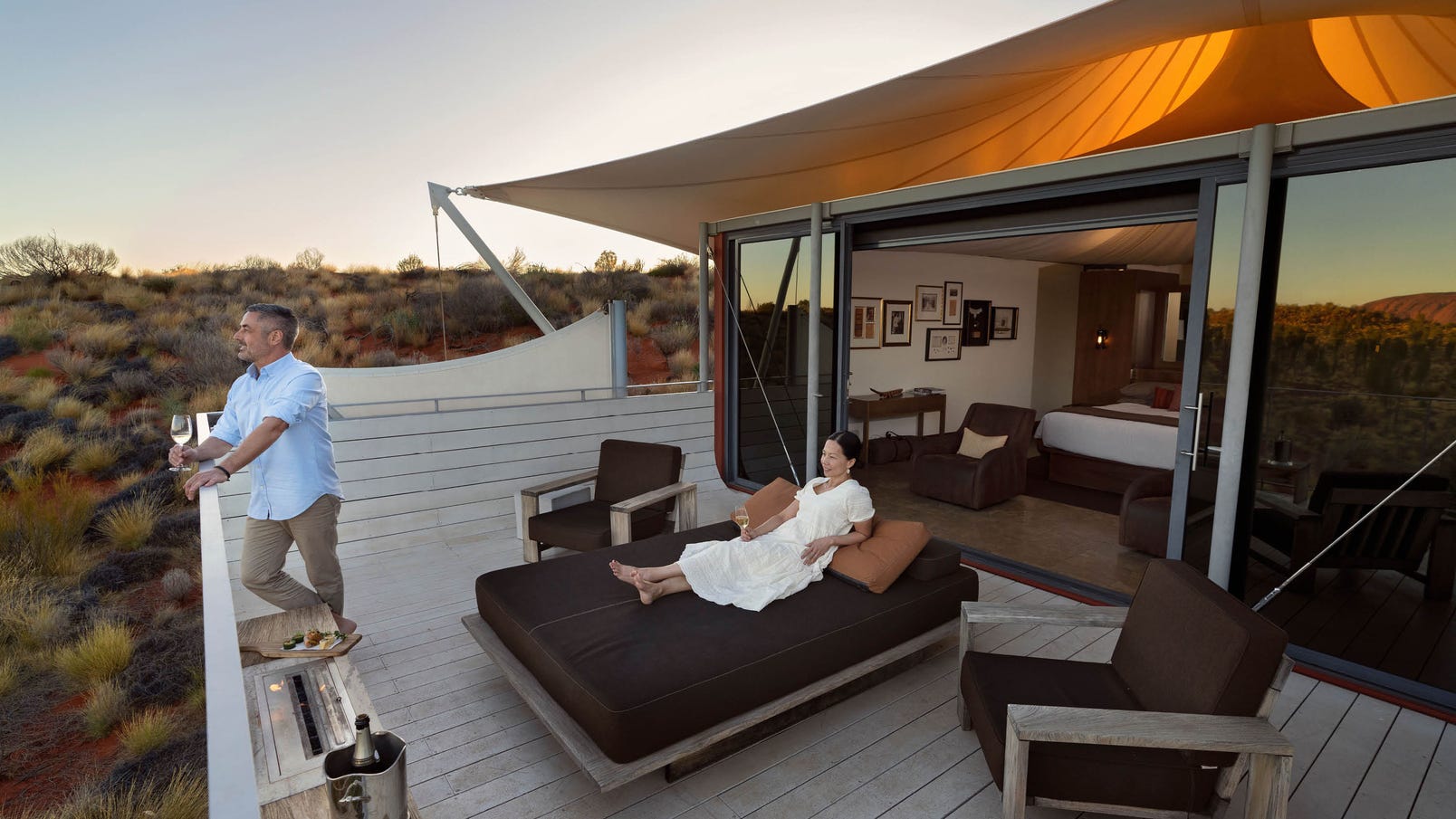 man having glass of wine on balcony while woman relaxes on sunbed at longitude 131 at uluru