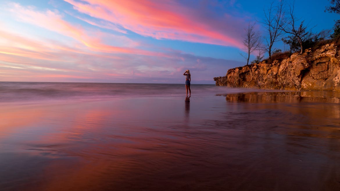 Girl standing on Casuarina Beach at sunset