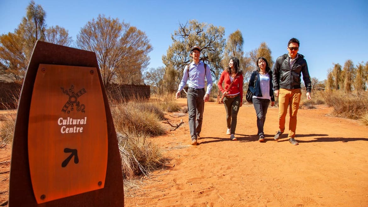 Visitors walking on red sand trail and a sign directing to Uluru Cultural Centre in the morning