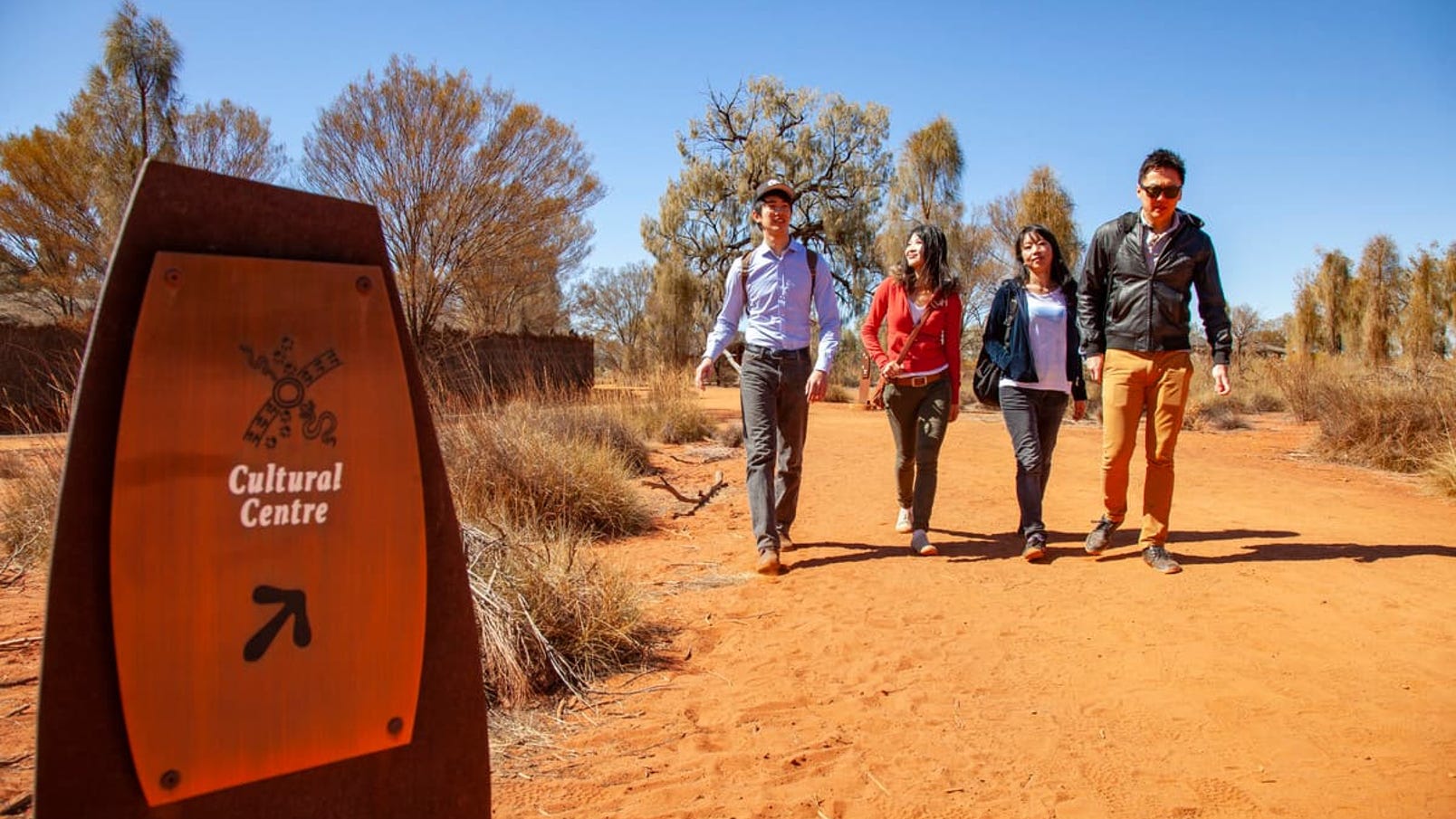 Visitors walking on red sand trail and a sign directing to Uluru Cultural Centre in the morning