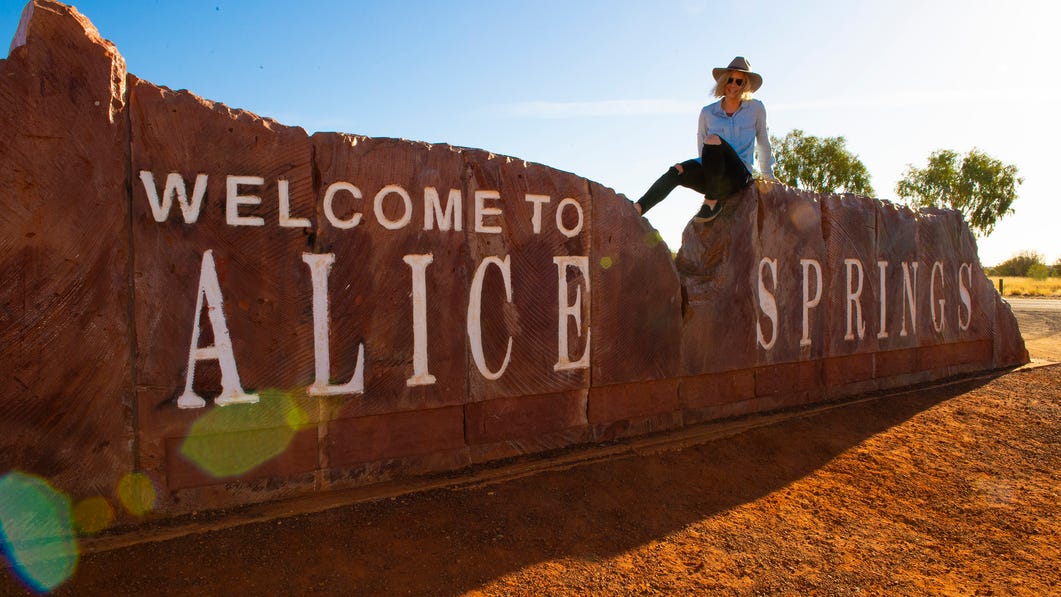 Woman sitting on the Welcome to Alice Springs sign