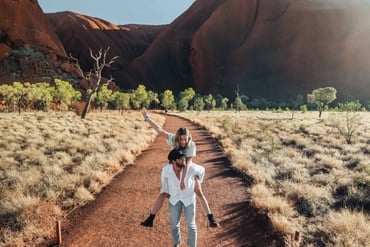A girl riding piggyback with her partner in front of Uluru