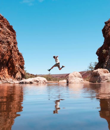 Man jumping over the water at Glen Helen Gorge
