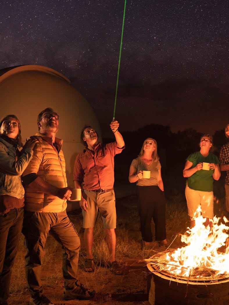 group standing around campfire looking up at the night sky with laser and dome in background at the earth sanctuary