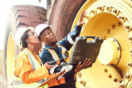 Man and a woman inspecting earth moving equipment on a work site.