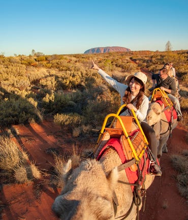 A girl pointing at Uluru whilst riding with Uluru Camel Tours