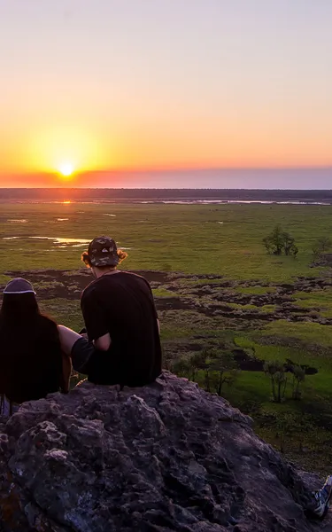 Three people sitting on a rock in Ubirr and watching the sunset