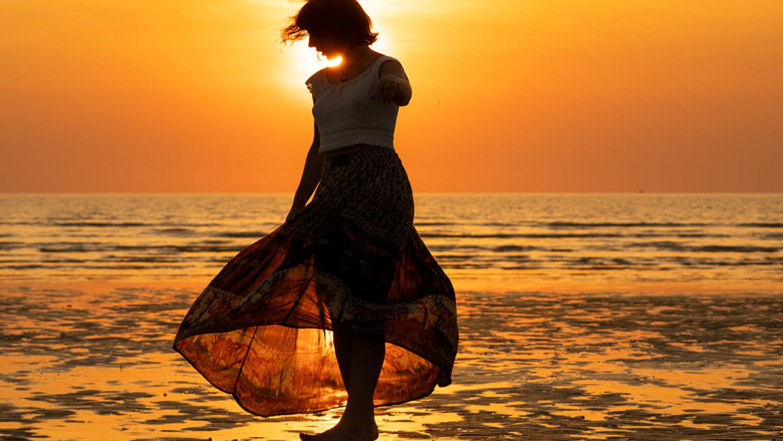 A woman in silhouette as she walks on the beach at sunset in Darwin