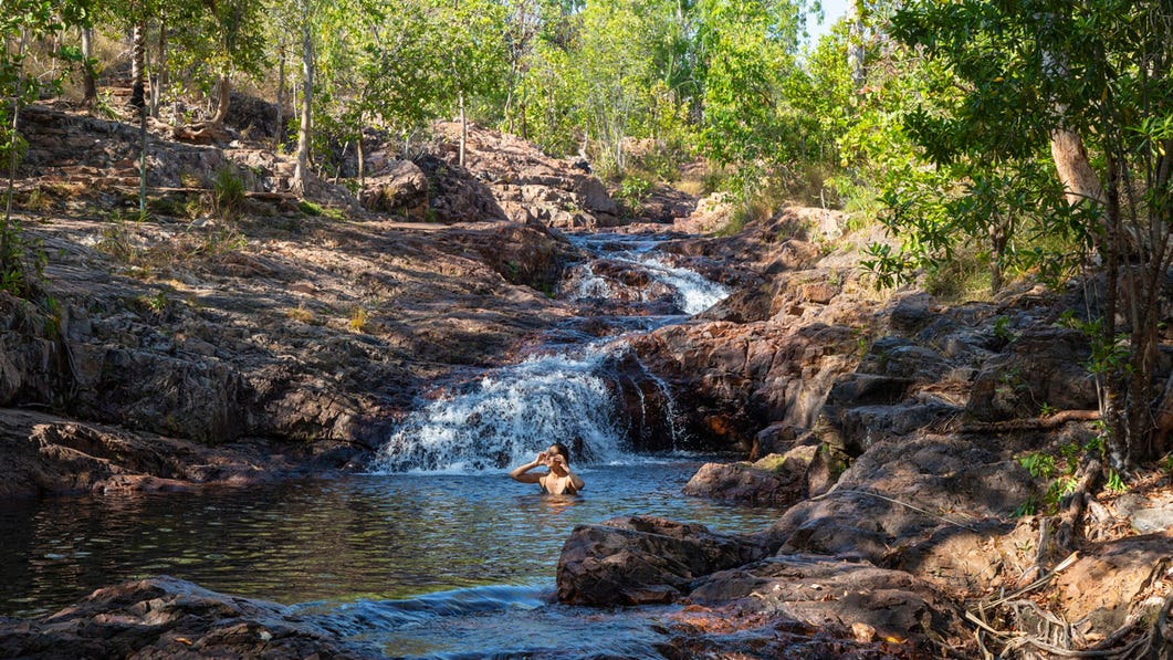 a woman swimming in the buley rockhole pool with water casading over the rocks behind her