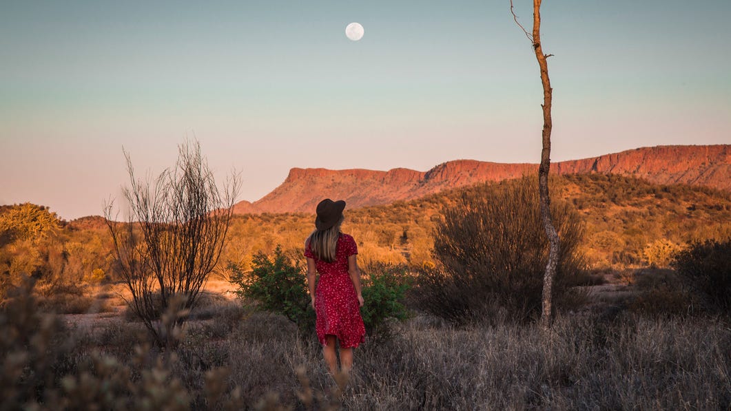 woman standing in the bush looking at the west macdonnell ranges