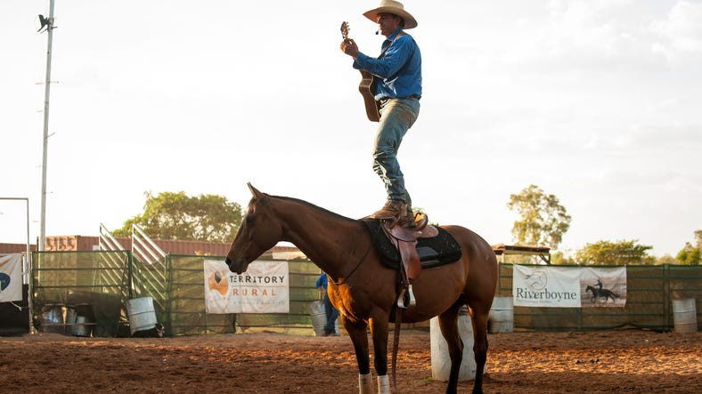 Man playing guitar standing on a horse