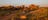 Looking down from above onto a campervan travelling on a sealed road through Devils Marbles Conservation Reserve, solar panels and surboard attached to its roof. To one side of the road, dotting the landscape, are the orange-ochre coloured boulders o
