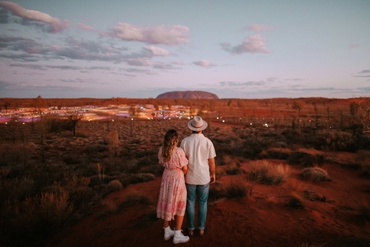 A couple holding hands in front of the Field of Light exhibition with Uluru in the background