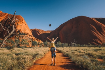A girl throwing her hat from atop her friend s shoulders in front of Uluru