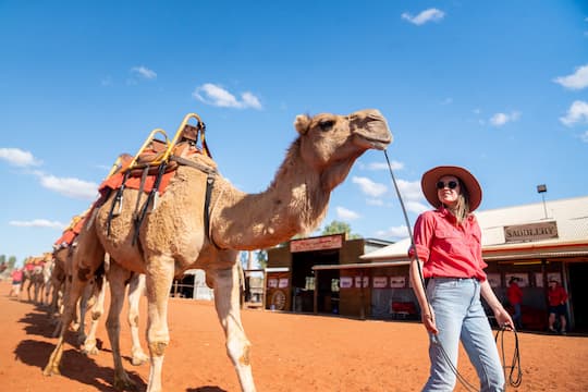 Woman walking a camel in the outback.