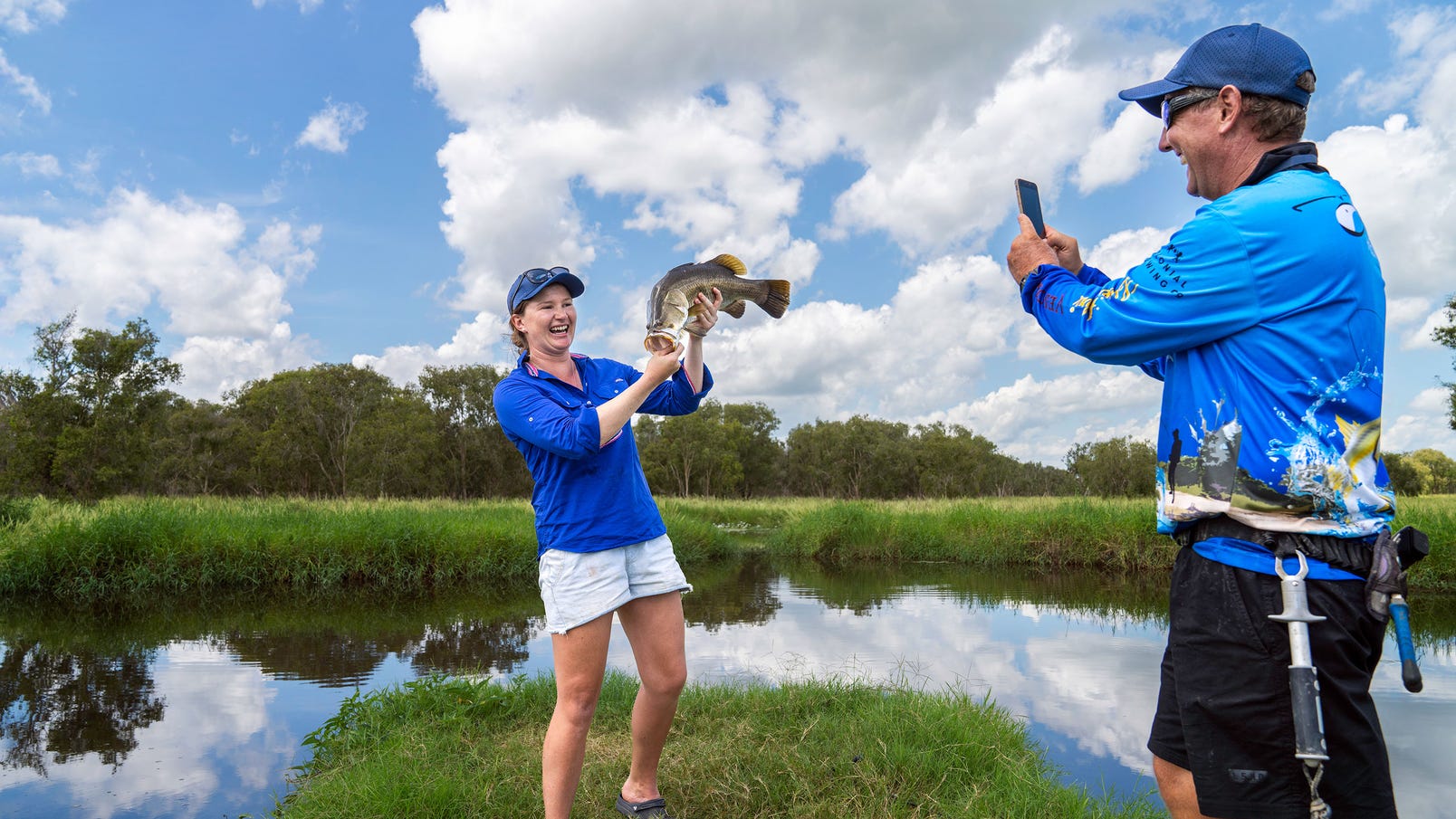 A woman holding a fish as man takes photo in Top End