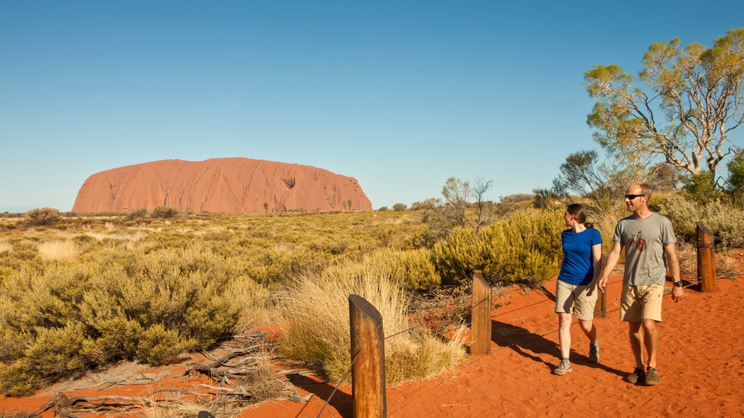 A couple walking in the area around Uluru with Uluru in the background