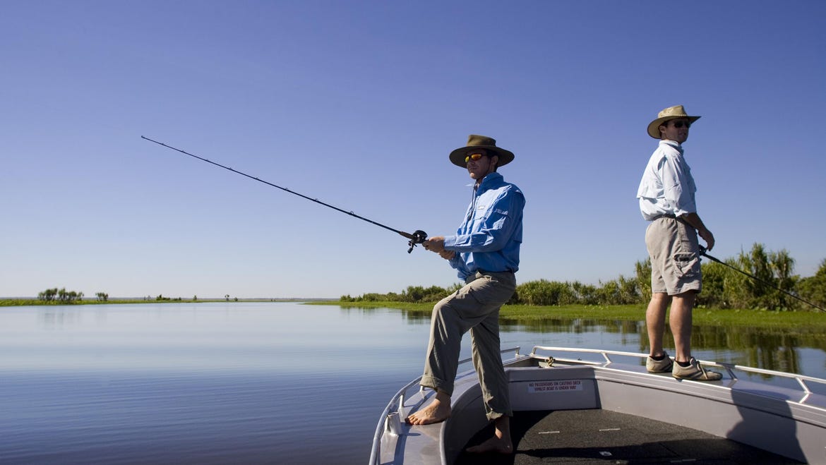 Two guys standing on the edge of their boat fishing in the Mary River