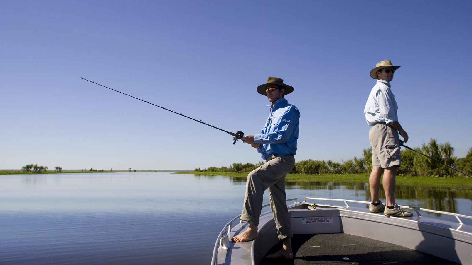 Two guys standing on the edge of their boat fishing in the Mary River