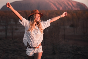 A woman standing with her arms raised in front of Uluru