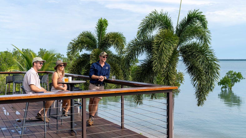 people standing on a deck next to the sea and palm trees
