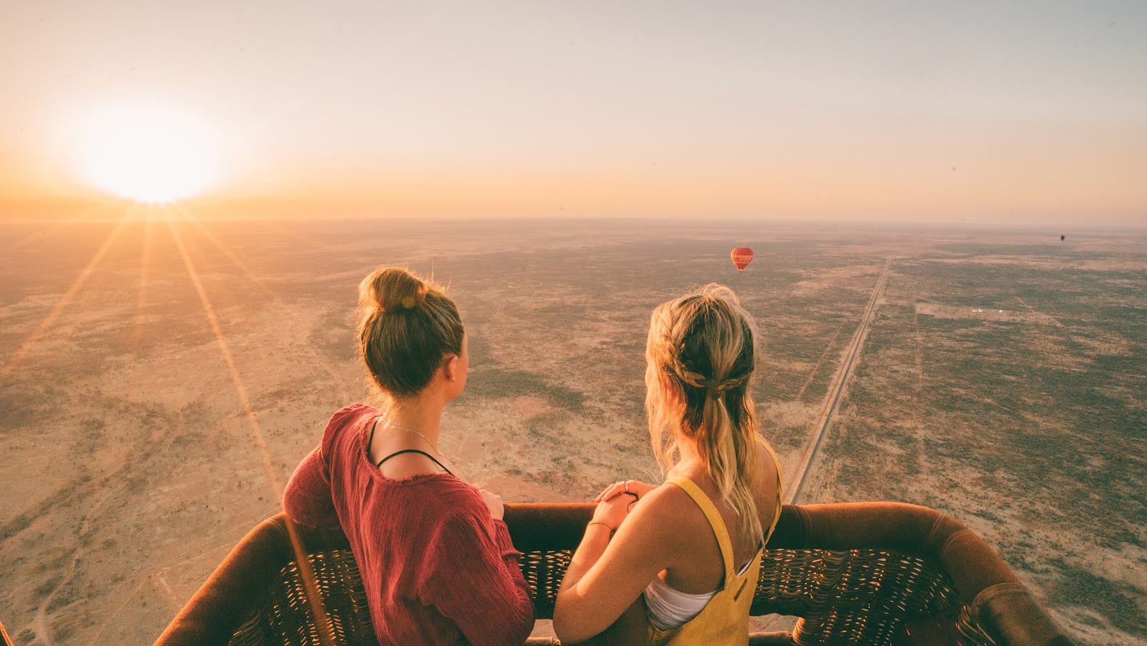 Two girls on a hot air balloon ride at sunrise looking at another balloon