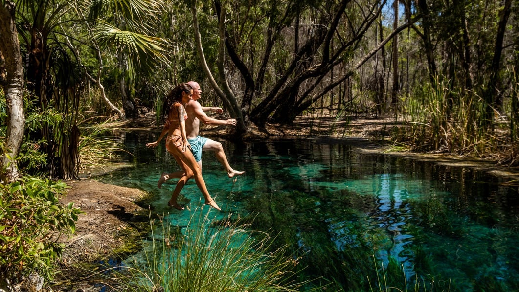 A couple jumping into the water in Bitter Springs