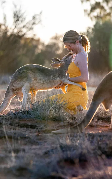 Woman in yellow dress feeding a kangaroo at a kangaroo santuary in Alice Springs