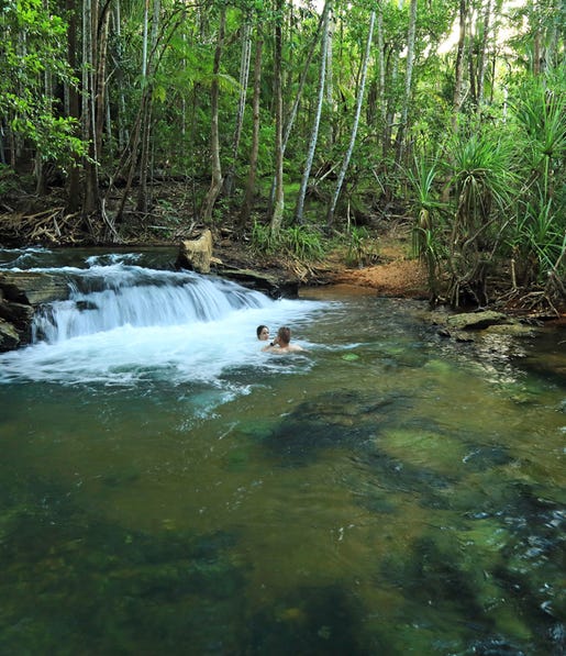 a couple floating in the water at berry springs next to water casading over a dropoff next to them
