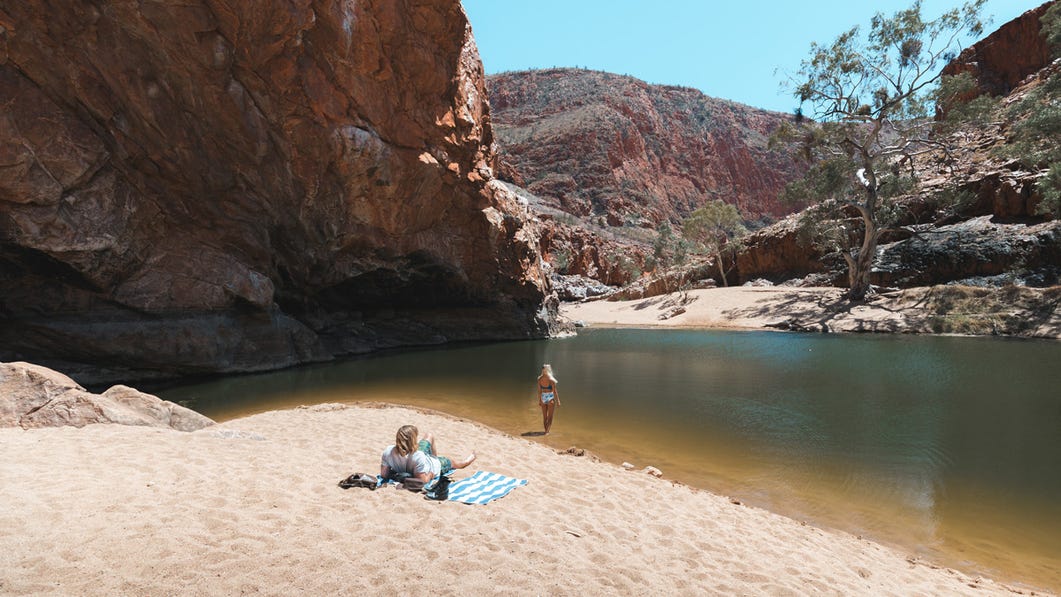 couple relaxing on the sand by the waters edge at ormiston gorge