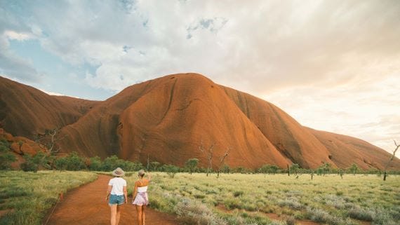Two friends walking on a path towards Uluru