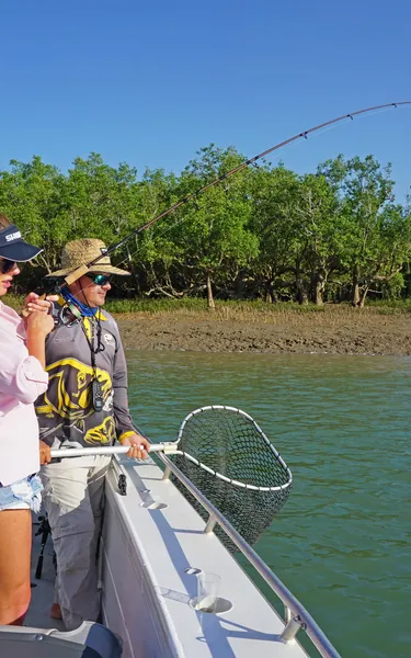 woman fishing from a boat with a man standing next to her holding a net